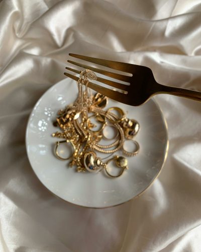 Exquisite gold jewelry elegantly displayed on a white plate with a fork, set against silk fabric.